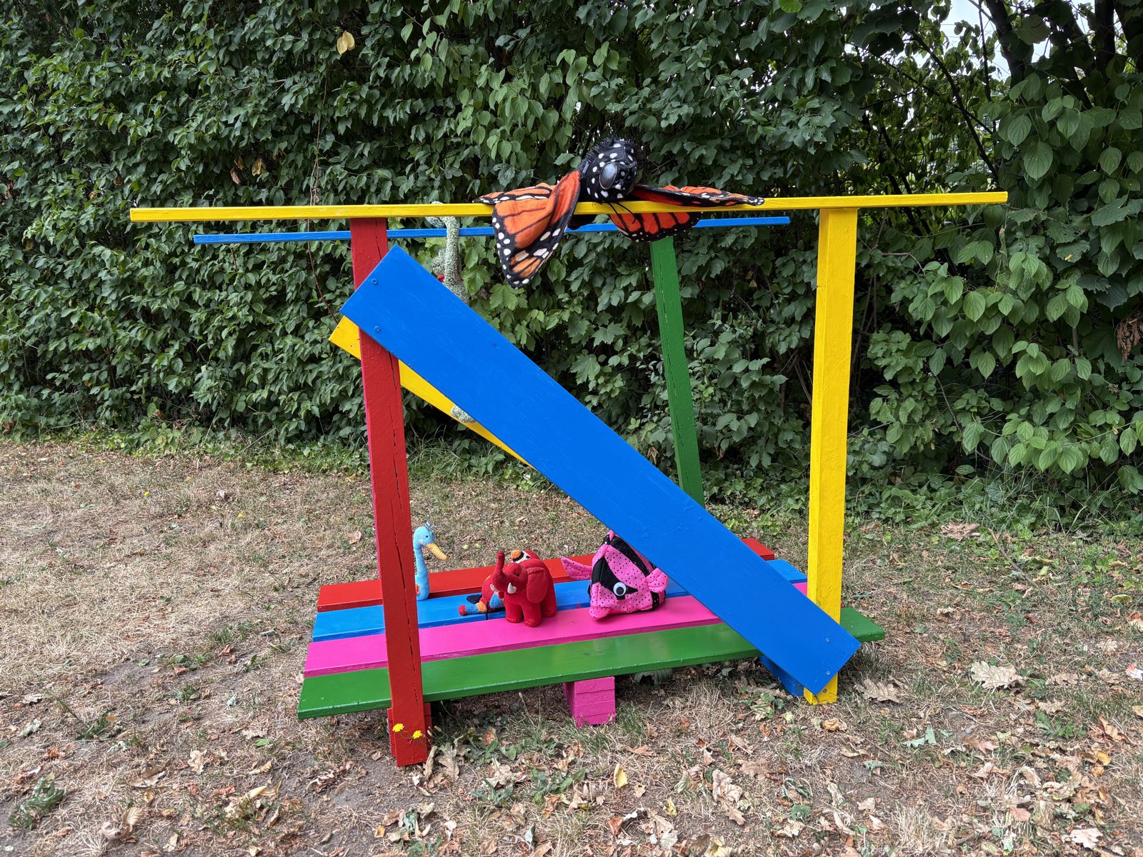 Die bunte Holzbrücke der Projektgruppe Einschulung auf der Wiese, oben sitzt ein großer Stoff-Schmetterling.