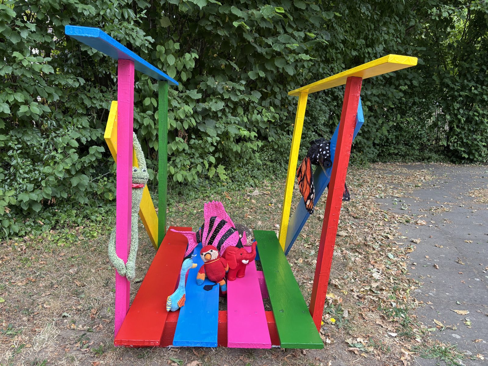 Die bunte Holzbrücke mit den Stofftieren der Geschichte: Schmetterling, Chamäleon, Papagei und Elefant.