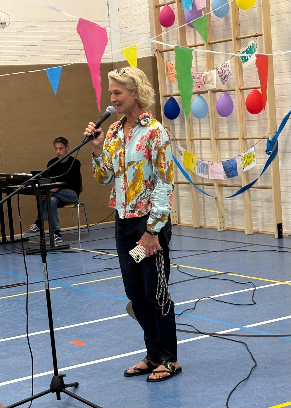 Begrüßung am Mikrofon vor bunten Wimpelketten und Luftballons in der Sporthalle.