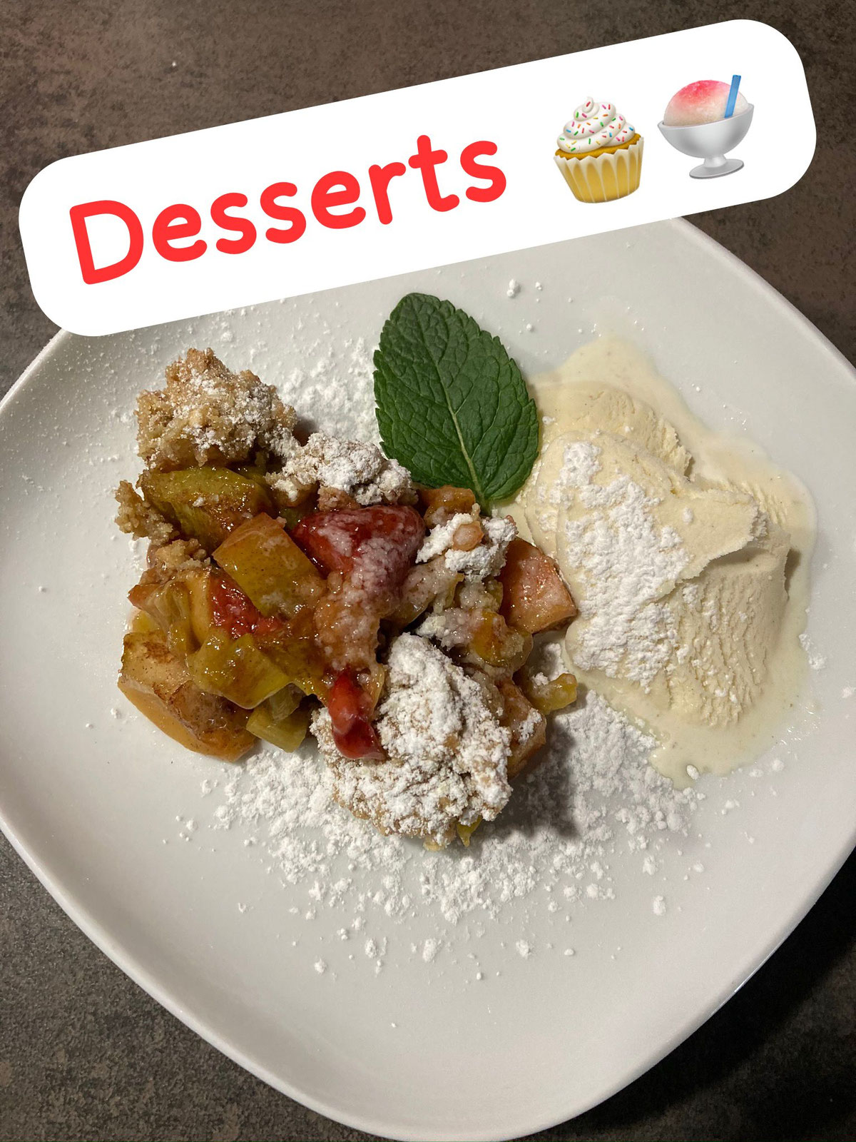 Dessertteller mit Streuseln, Früchten, Eis, Puderzucker und einem Minzblatt