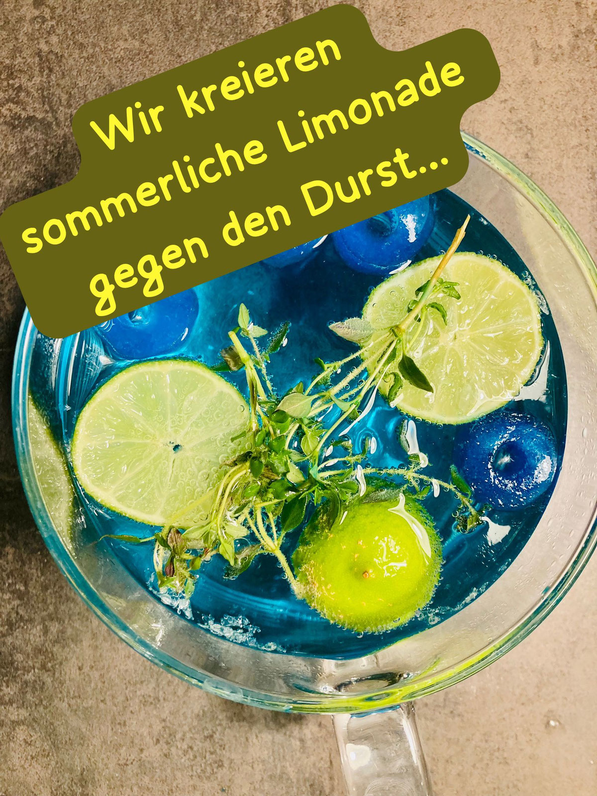 Glaskanne mit blauer Limonade, Limettenscheiben und Kräutern
