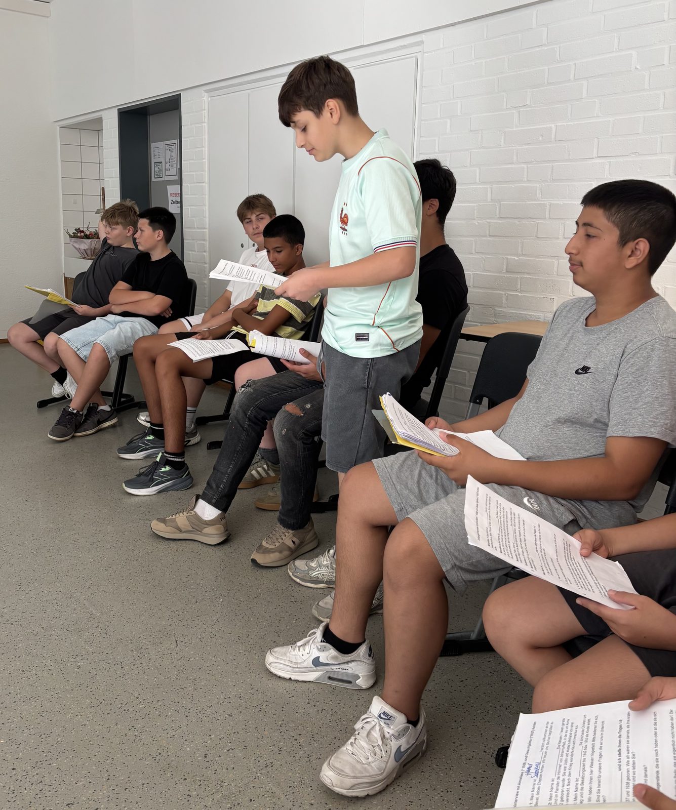 Schüler der Klasse 7a sitzen im Kreis und lesen ihre vorbereiteten Fragen von Arbeitsblättern ab.